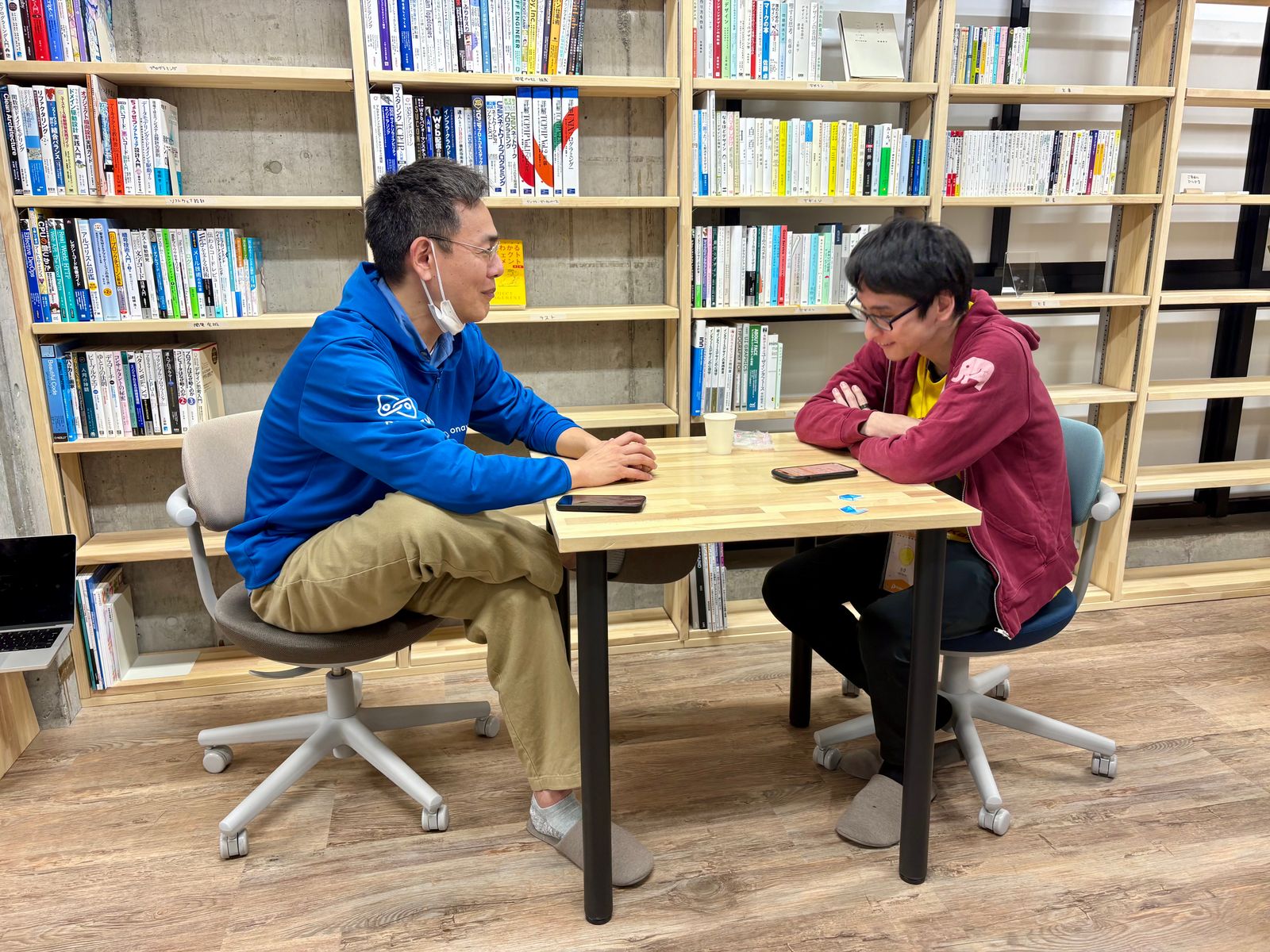 技術書ライブラリーで話し込むエンジニア二人の写真