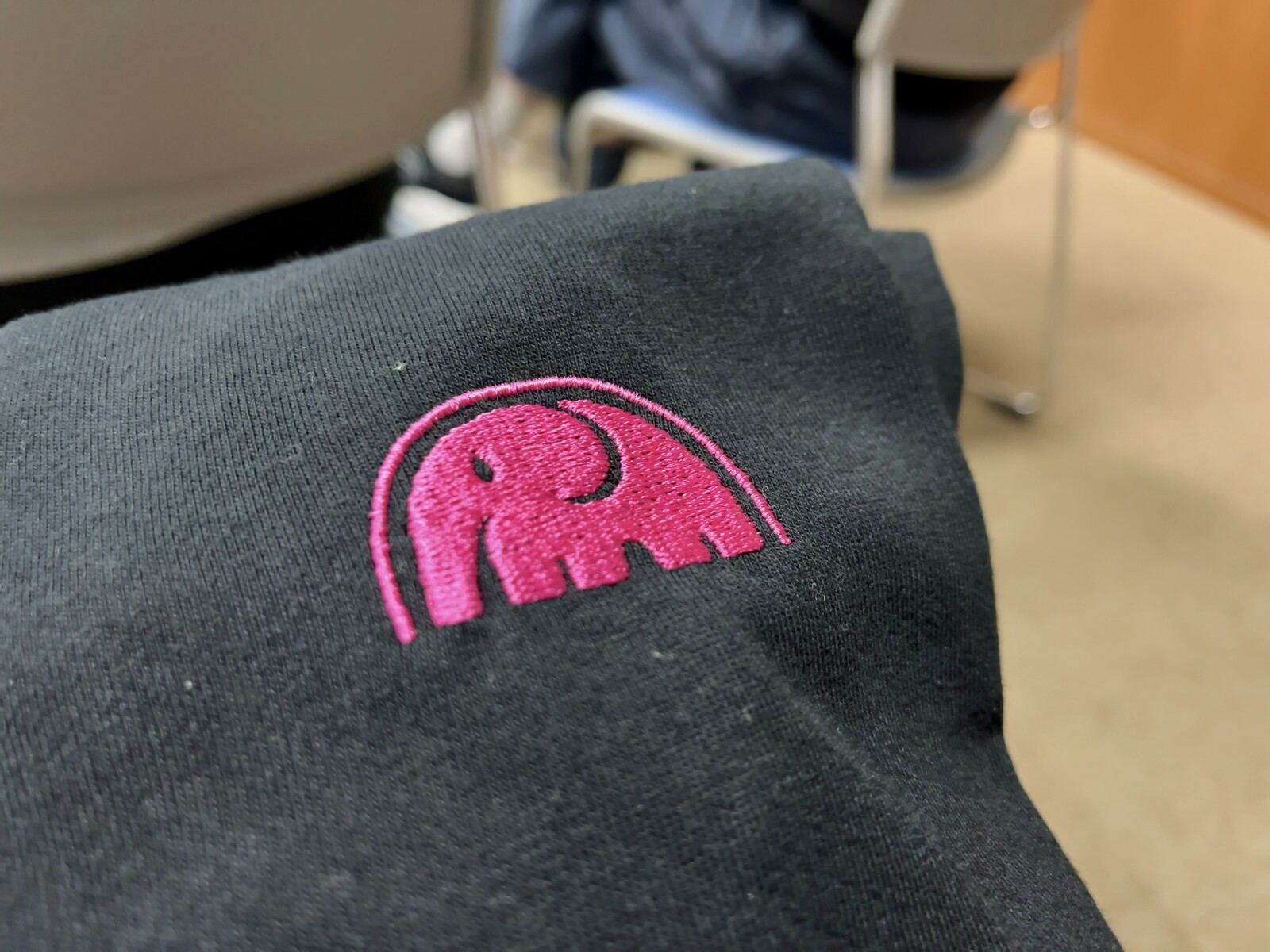 PHPカンファレンス小田原2024のノベルティTシャツの写真。ピンクのロゴが刺繍で入っている